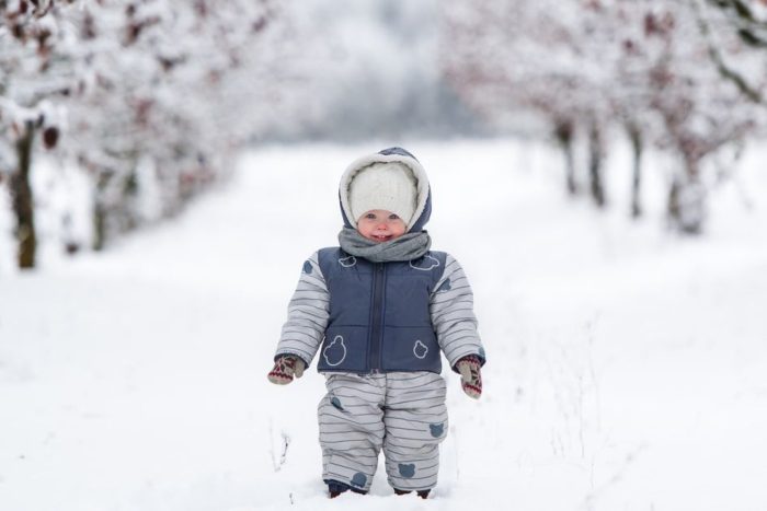 A bundled-up toddler in a winter snowsuit and hat walking through a snowy path