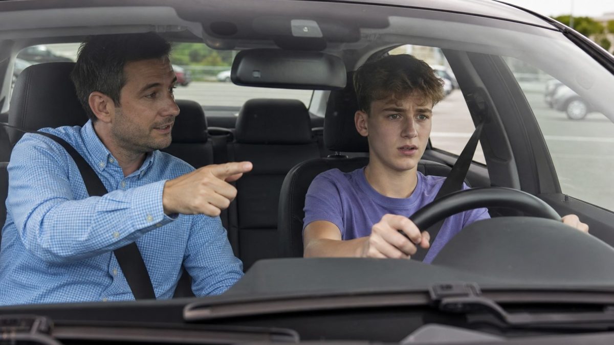 A driving instructor giving guidance to a student driver behind the wheel
