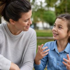 A parent attentively listening to a child speaking expressively outdoors