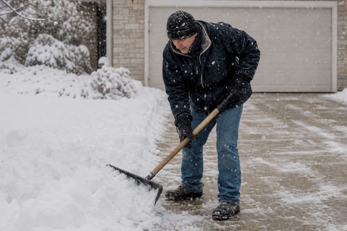 A person shoveling snow off a residential driveway during a snowfall