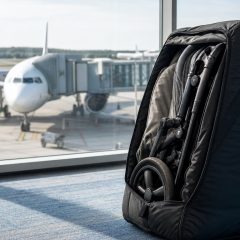 A folded stroller in a padded travel bag at an airport gate with a plane visible outside